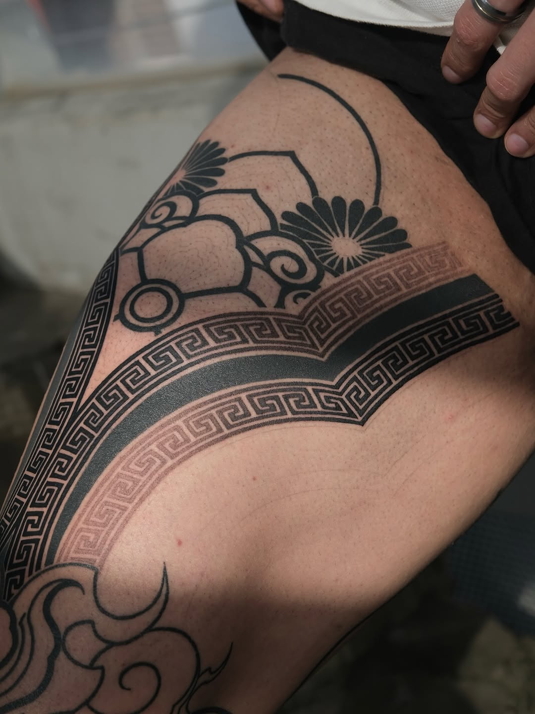 Ornamental geometric tattoo on upper arm featuring symmetrical patterns, Greek key borders, and stylized fan motifs in black ink.
