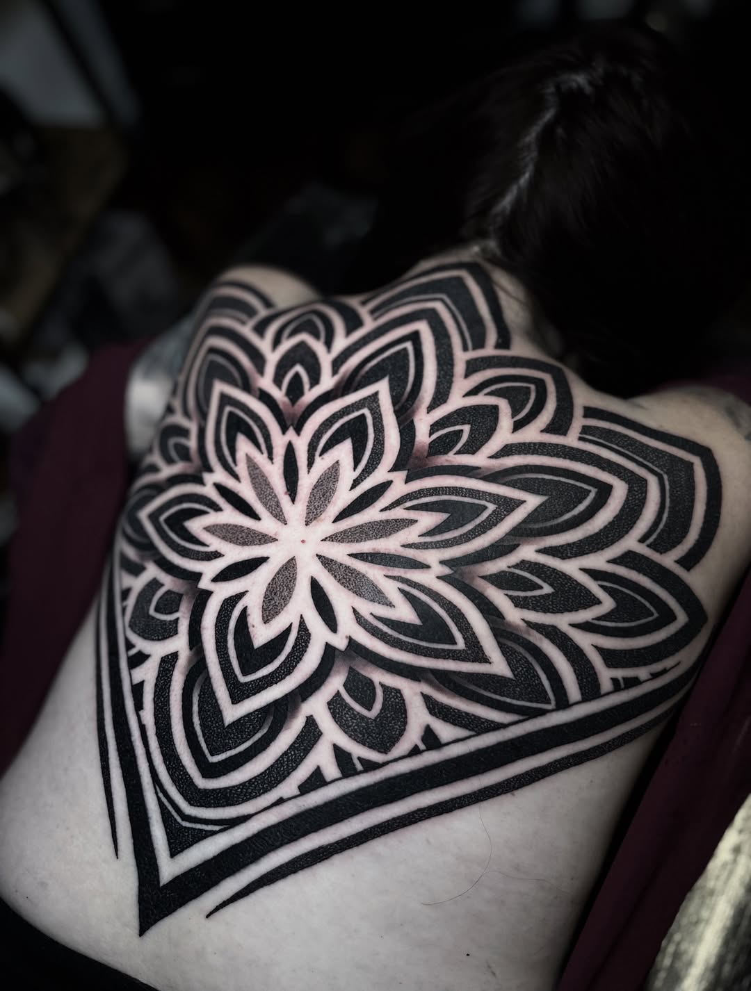 Black and white mandala-style geometric tattoo with concentric nested petals and symmetrical linework on the shoulder.