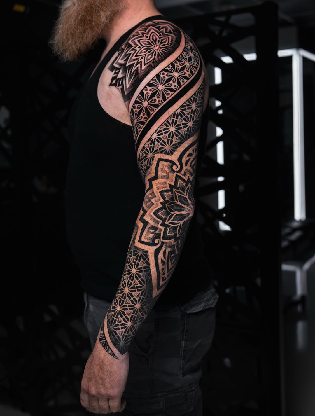 Full sleeve mandala and geometric pattern tattoo with intricate symmetrical dotwork and star motifs in black and orange on arm and leg.