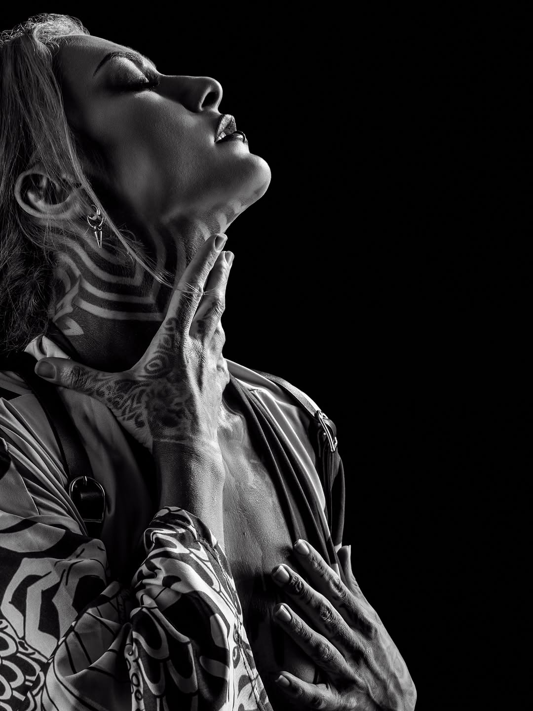 Black and grey photorealistic portrait tattoo on upper chest and shoulder with zebra stripe patterned garment, shown in profile against dark background.