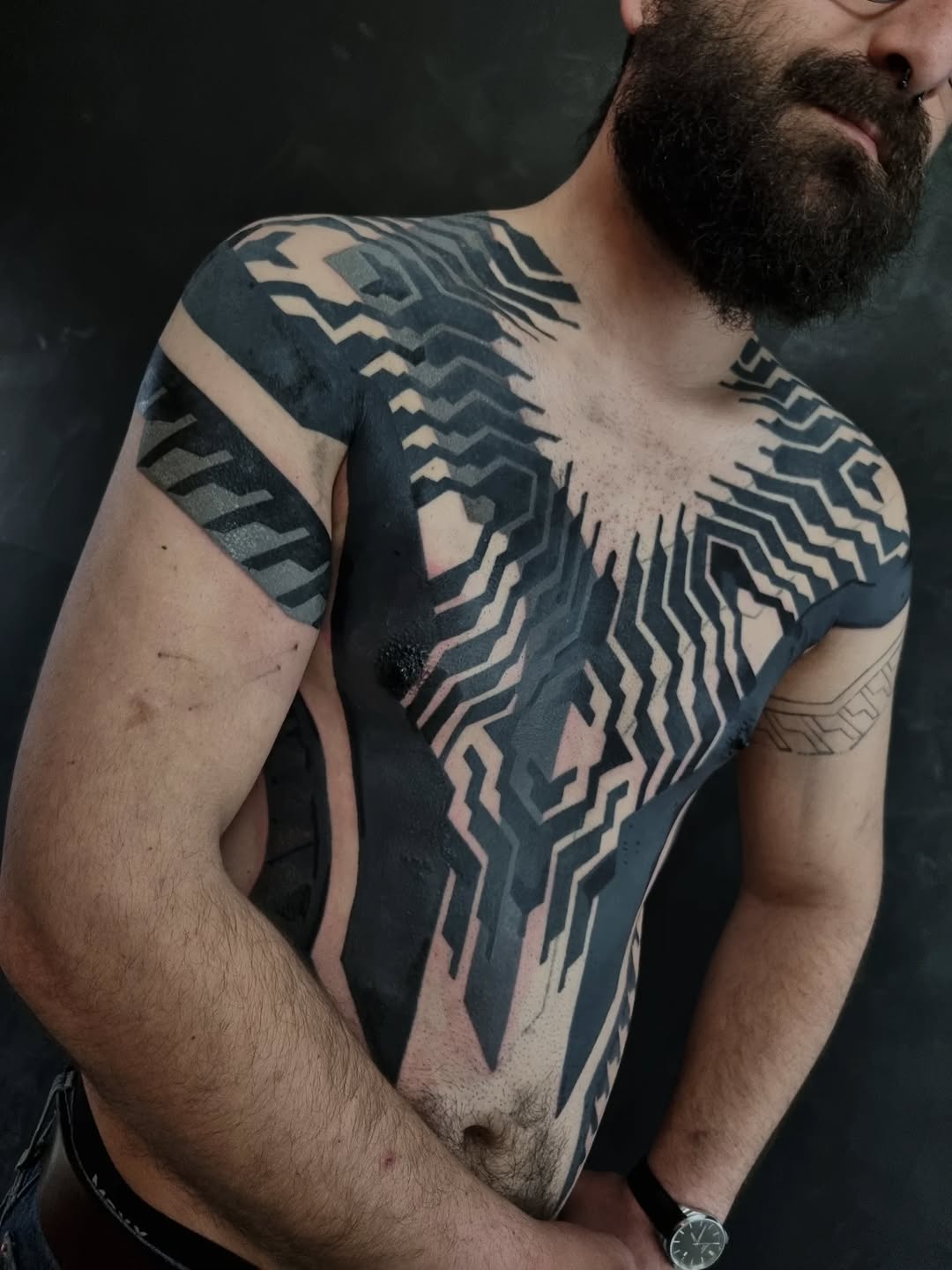 Large-scale geometric tattoo with precise angular linework and symmetrical patterns covering chest and shoulders in black ink.