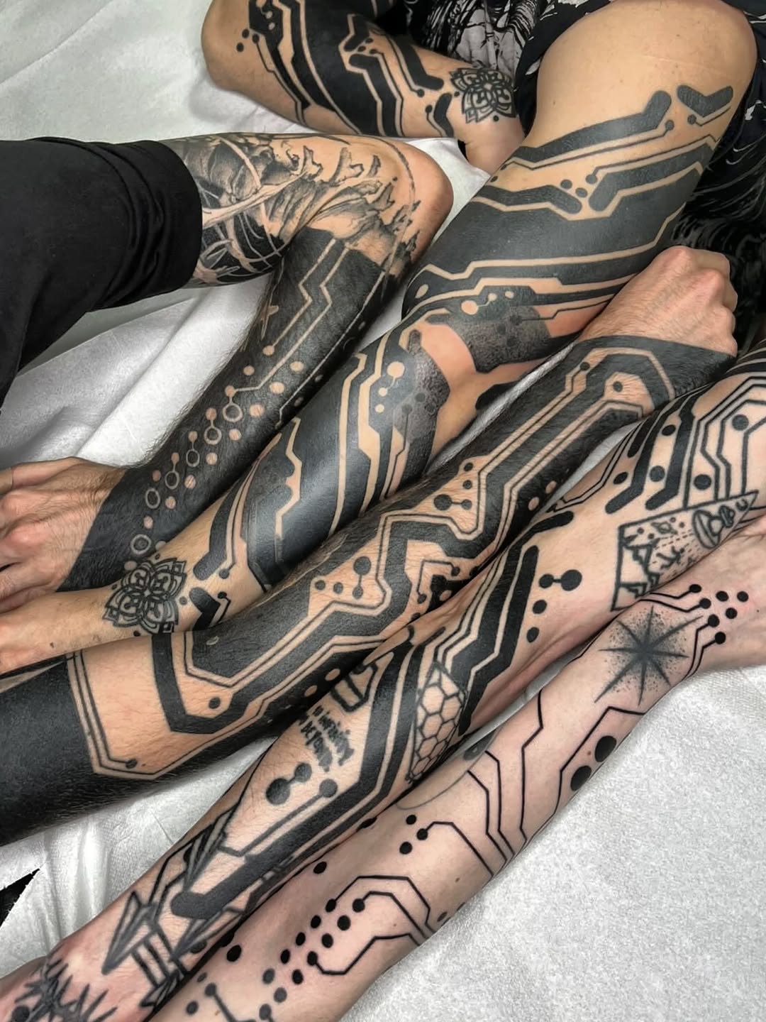 Multiple arms displaying circuit board and tech-inspired geometric linework with symmetrical patterns and dotwork stippling.