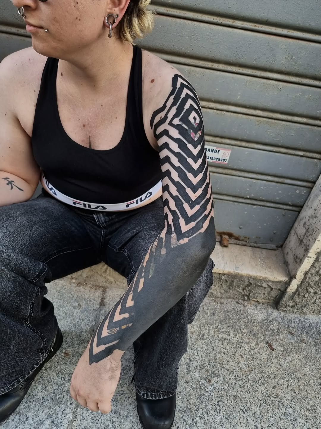 Large-scale geometric chevron pattern in black and skin-tone negative space covering the entire forearm.