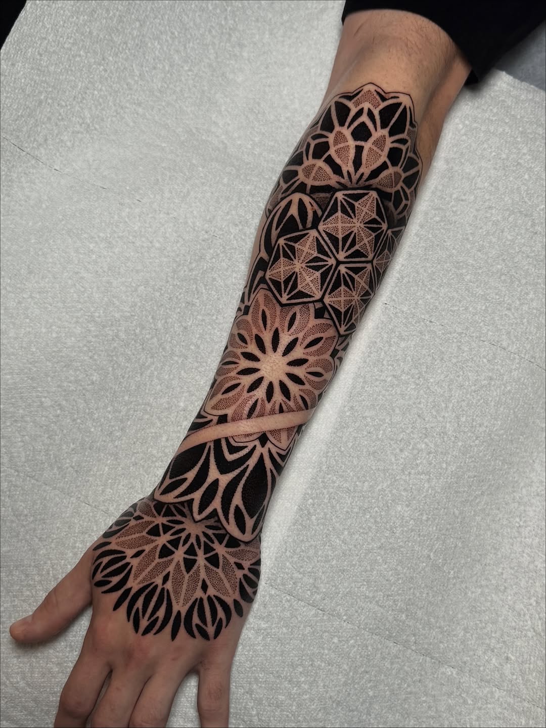 Full forearm sleeve featuring symmetrical mandala and geometric floral patterns in black dotwork and linework.