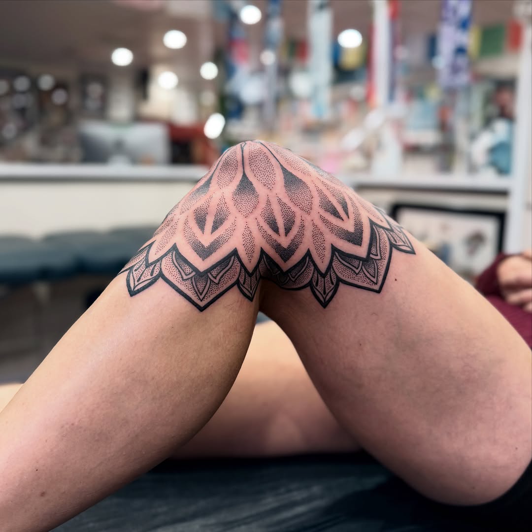Symmetrical mandala-style dotwork tattoo wrapping around both thighs with intricate petal and geometric layering.