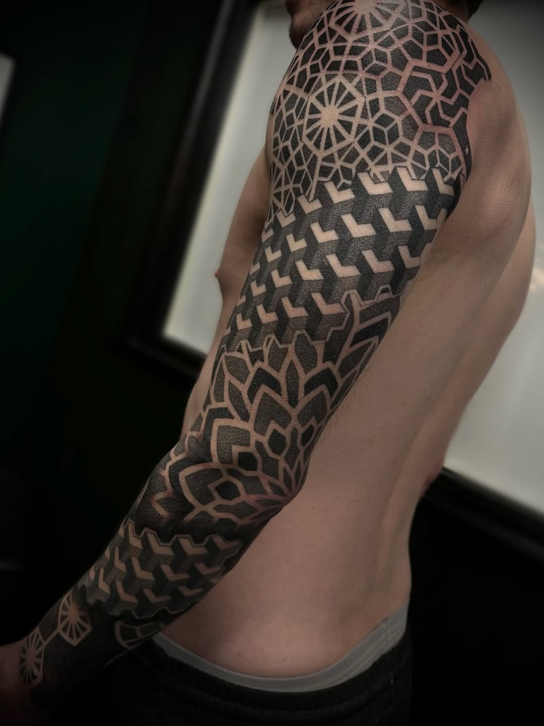 Full sleeve geometric mandala and interlocking pattern tattoo in black ink with dotwork and symmetrical linework on arm.