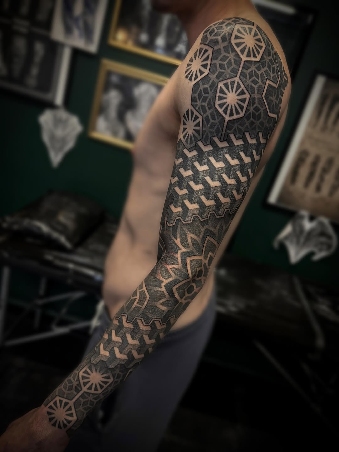 Full-sleeve geometric tattoo with mandala patterns, starburst motifs, and symmetrical ornamental linework in black and grey on forearm and upper arm.