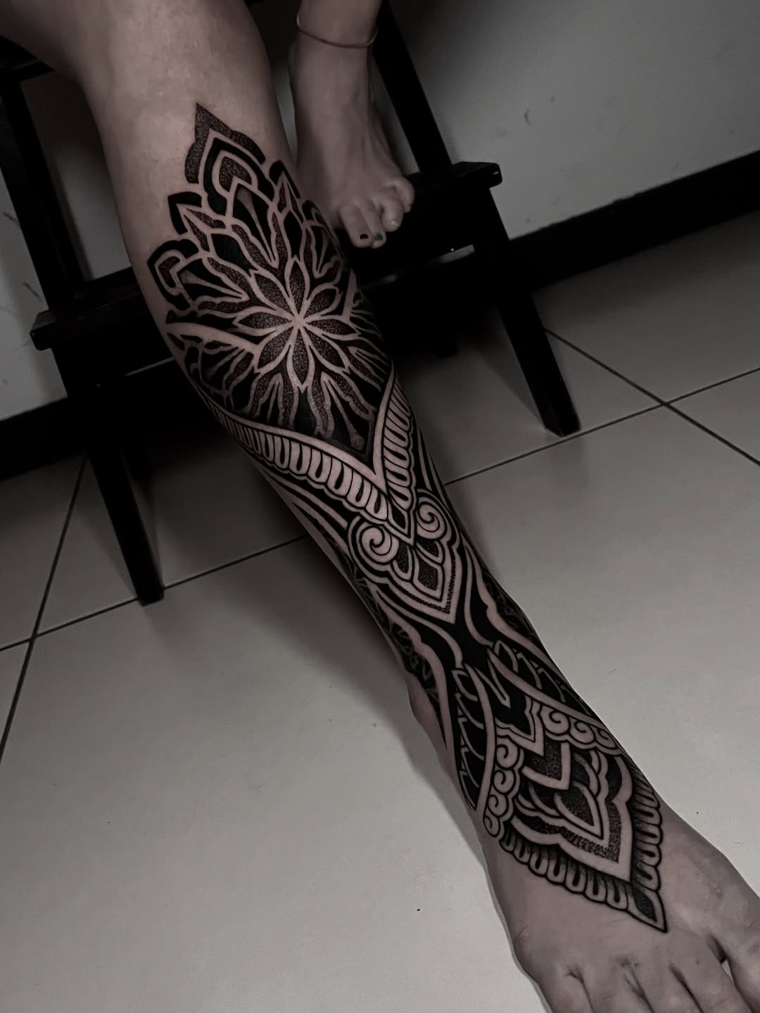 Intricate mandala and ornamental geometric linework tattoo extending from thigh down the leg with symmetrical patterning.