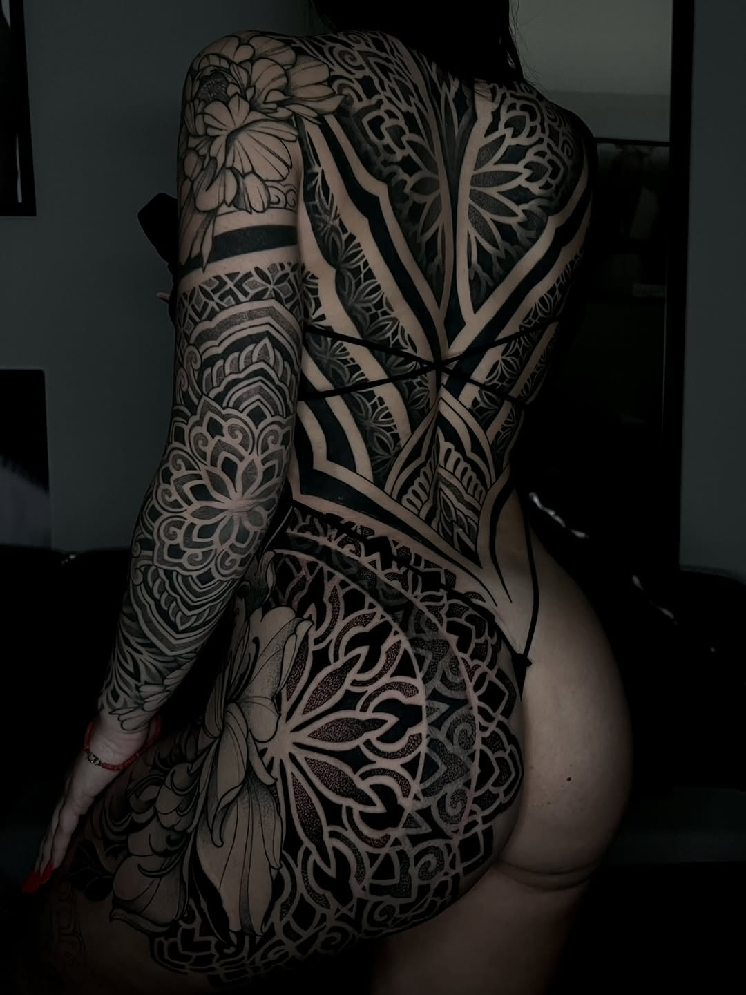 Intricate geometric and mandala patterns with floral elements covering the back and arm in black and grey linework.