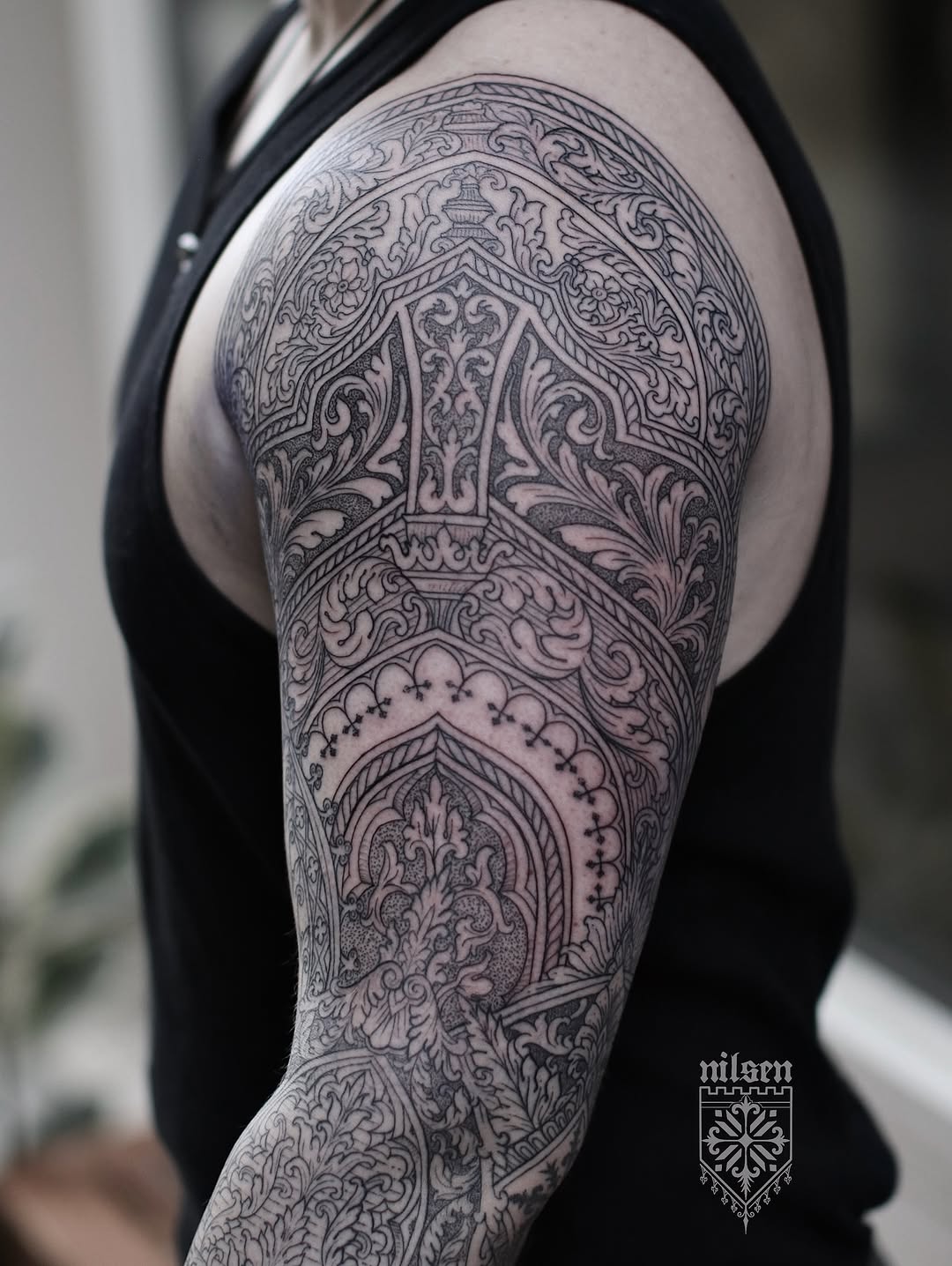 Ornate mandala-inspired chest and sleeve tattoo with symmetrical filigree scrollwork, architectural elements, and dotwork detail.