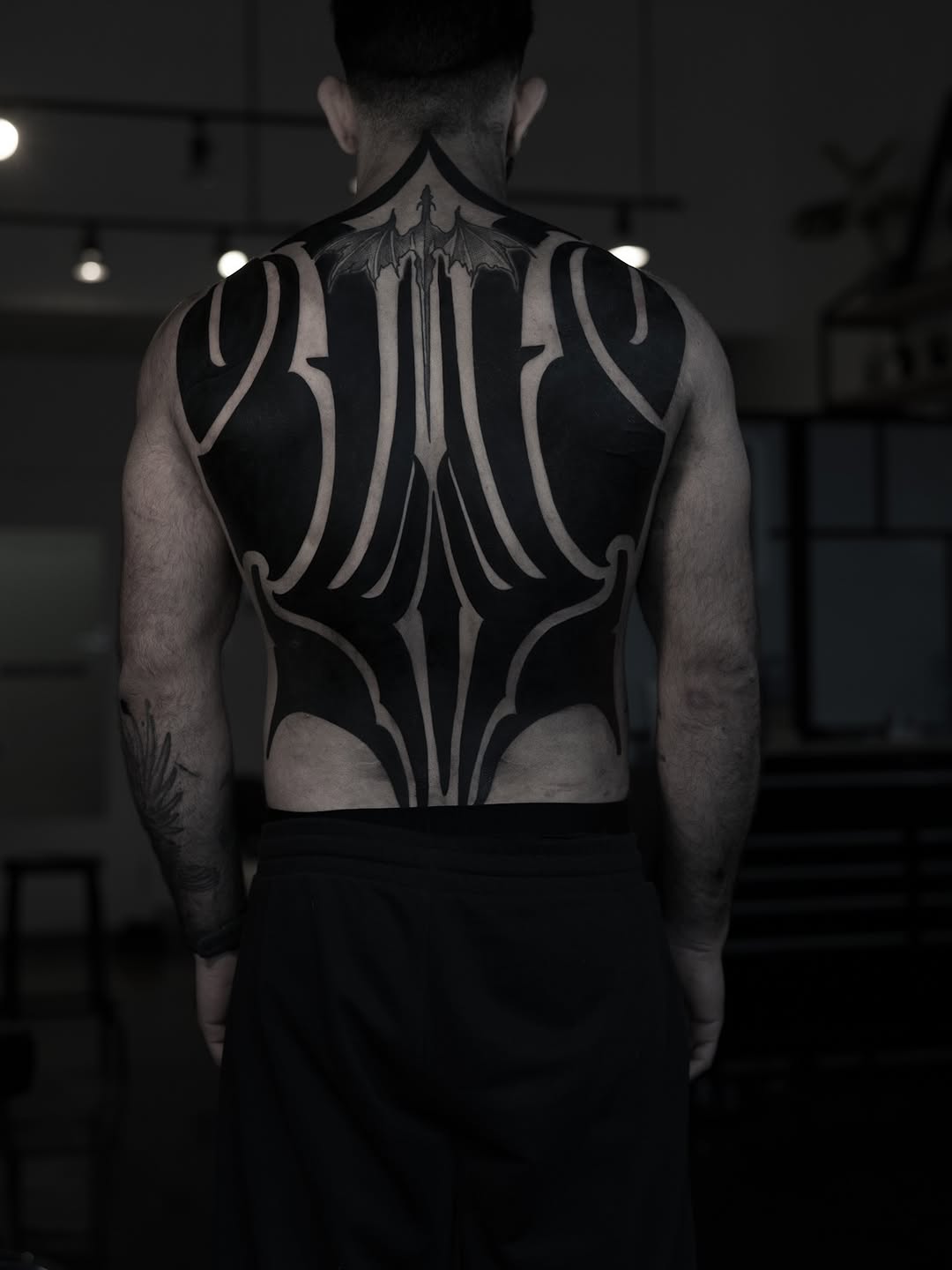 Large-scale symmetrical geometric back piece with ornamental linework, curved bands, and central spire motif in black ink.