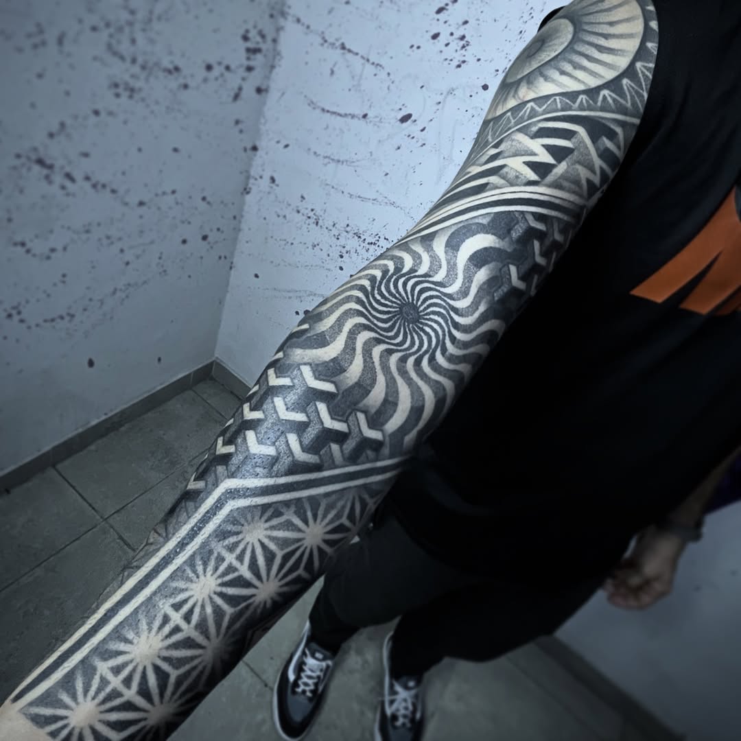 Full sleeve geometric tattoo with symmetrical mandalas, spirals, wave patterns, and ornamental linework in black and grey.