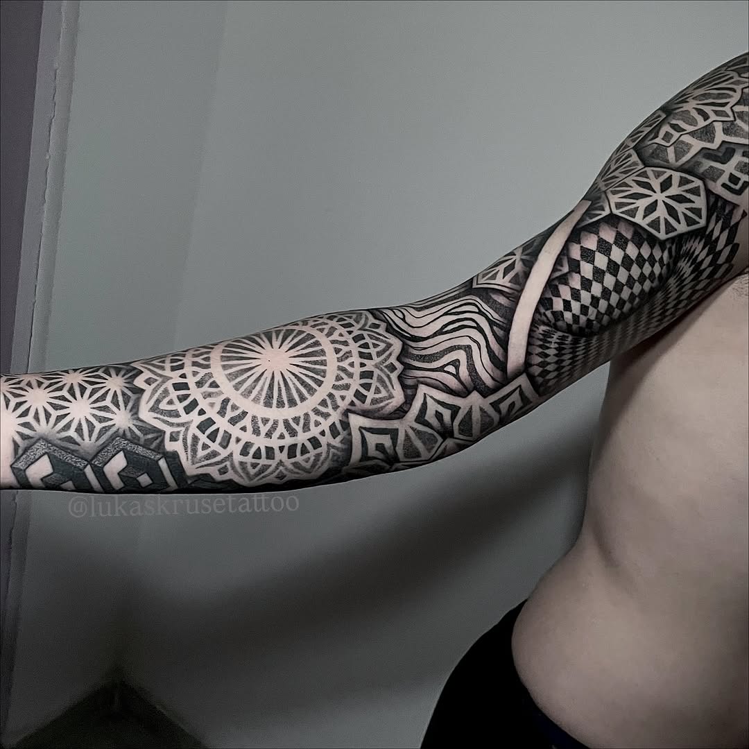 Full sleeve tattoo featuring intricate geometric mandalas, dotwork patterns, and symmetrical ornamental designs in black ink on the forearm and upper arm.