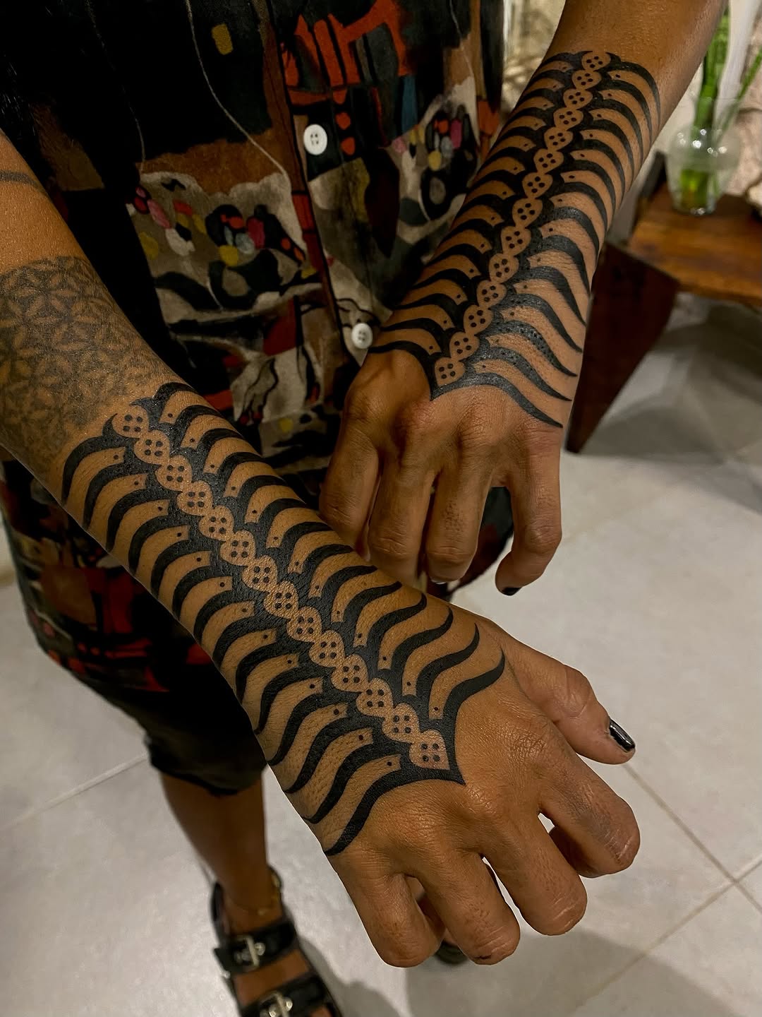 Symmetrical dotwork and curved line pattern covering both forearms in black ink, geometric ornamental design.
