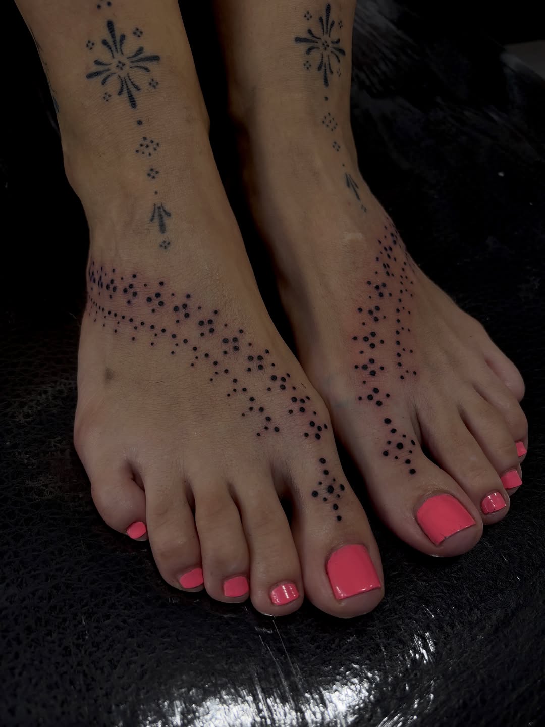 Dotwork stippling pattern covering feet and ankles with starburst designs on shins, pink nail polish.