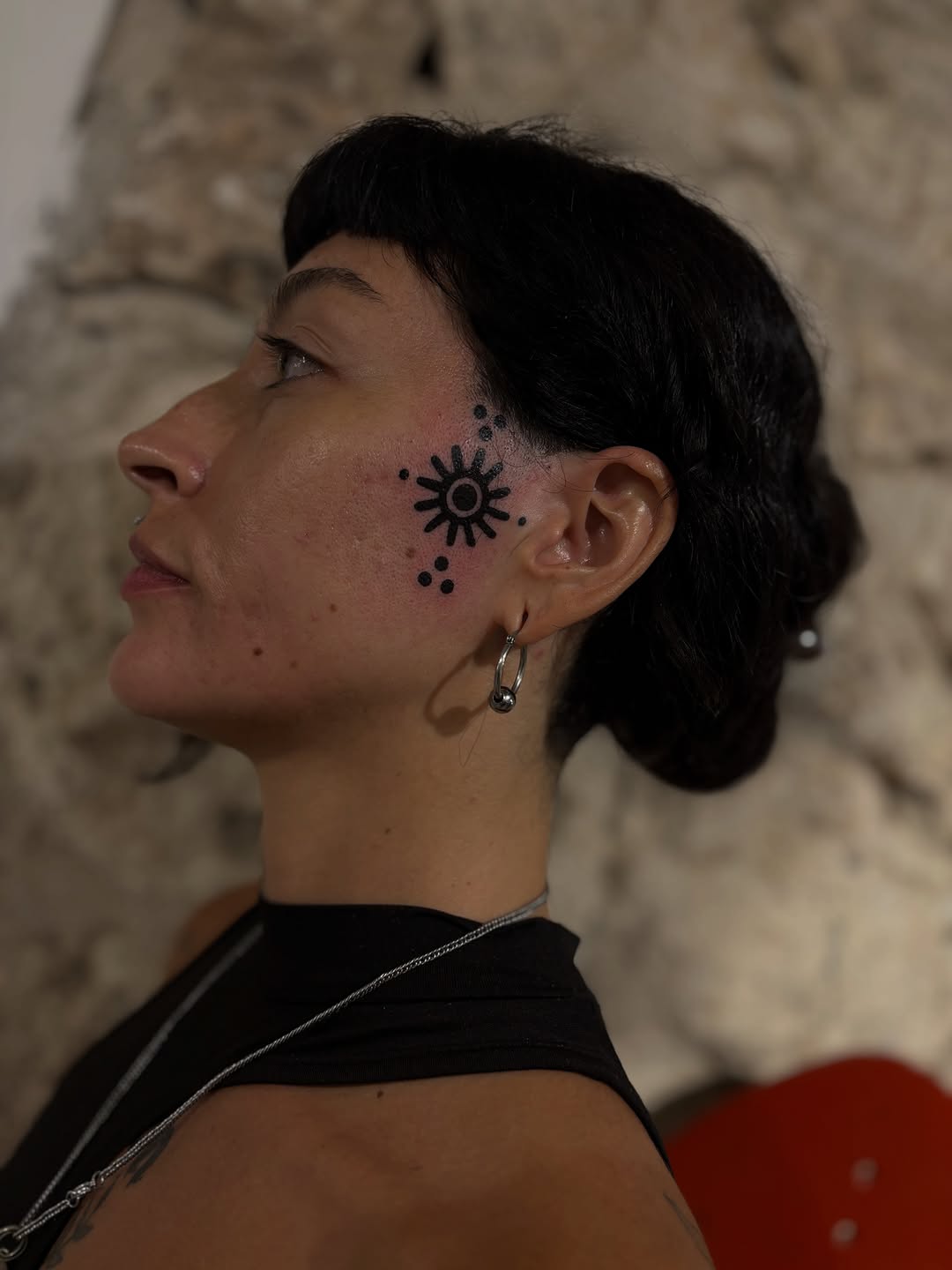 Sun with radiating lines and dotwork dots arranged vertically on the cheek near the ear.