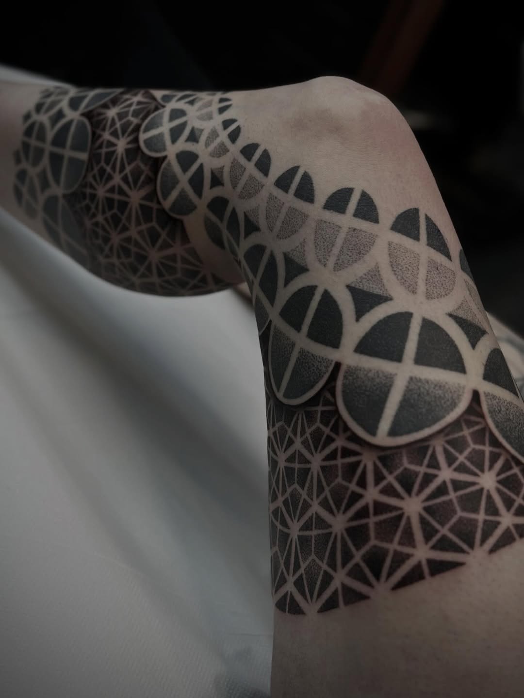 Geometric mandala-style tattoo with precise linework, dotwork stippling, and symmetrical circular patterns covering the upper arm and shoulder.