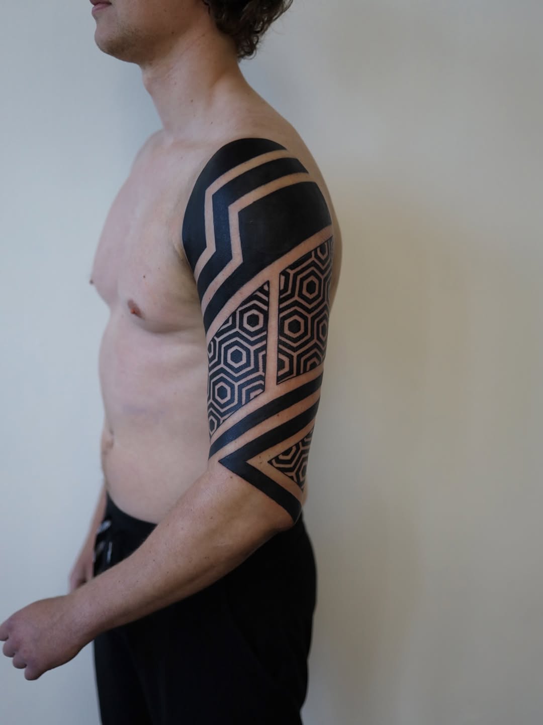 Geometric sleeve tattoo with hexagonal pattern, chevron bands, and triangular motifs in black ink on right shoulder and arm.