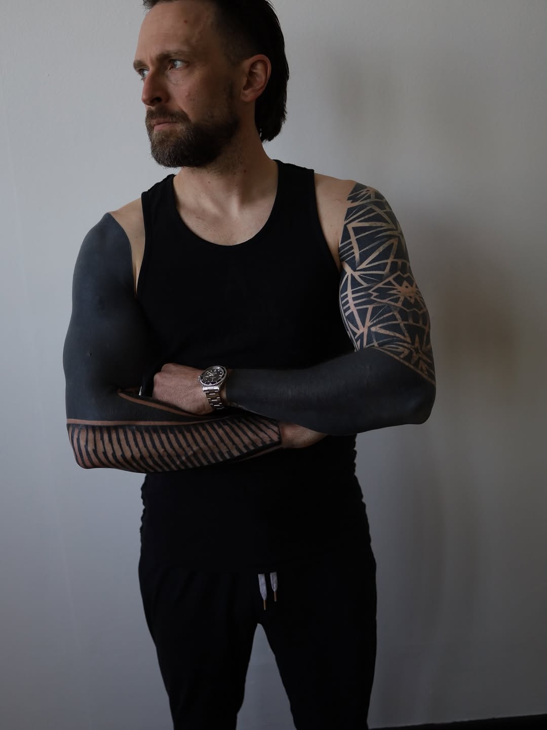 Geometric line-work tattoos covering both arms with angular patterns and symmetrical designs in black ink.