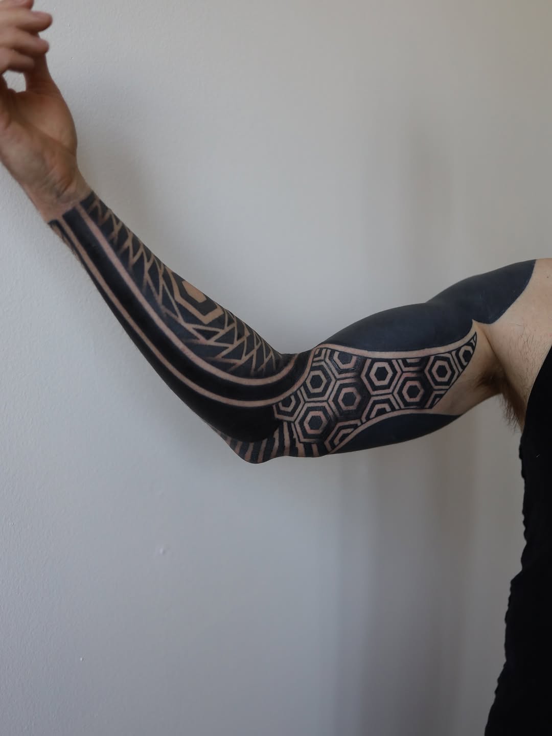 Geometric full-sleeve tattoo with symmetrical patterns, hexagonal motifs, and linear band designs wrapping the forearm.