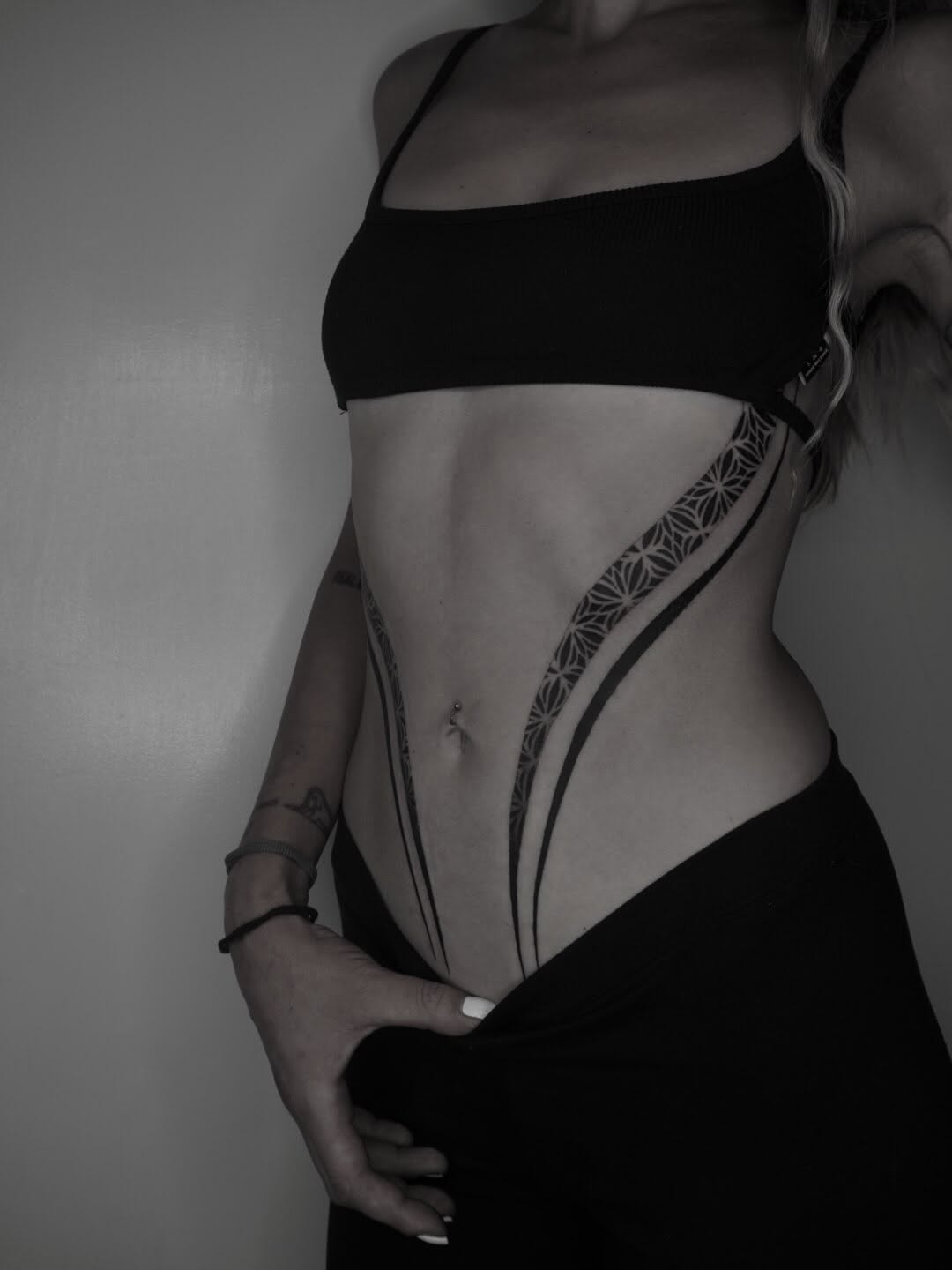 Geometric floral pattern with ornamental linework on hip and lower abdomen area in black ink.