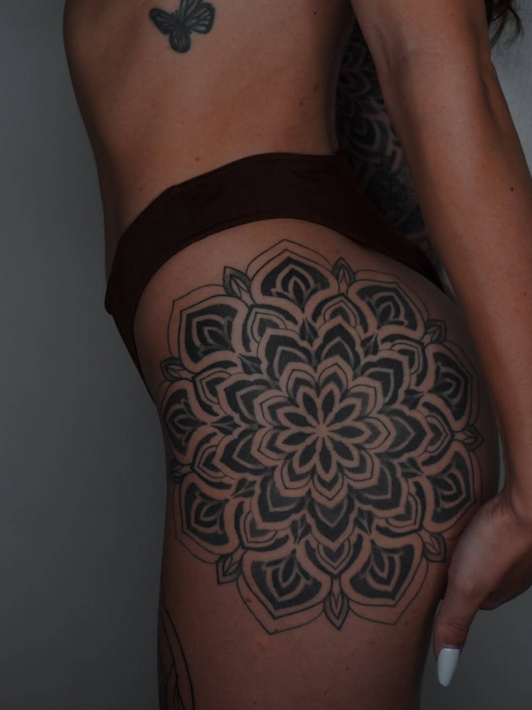 Intricate mandala with concentric petal patterns and symmetrical geometric layering on the thigh.