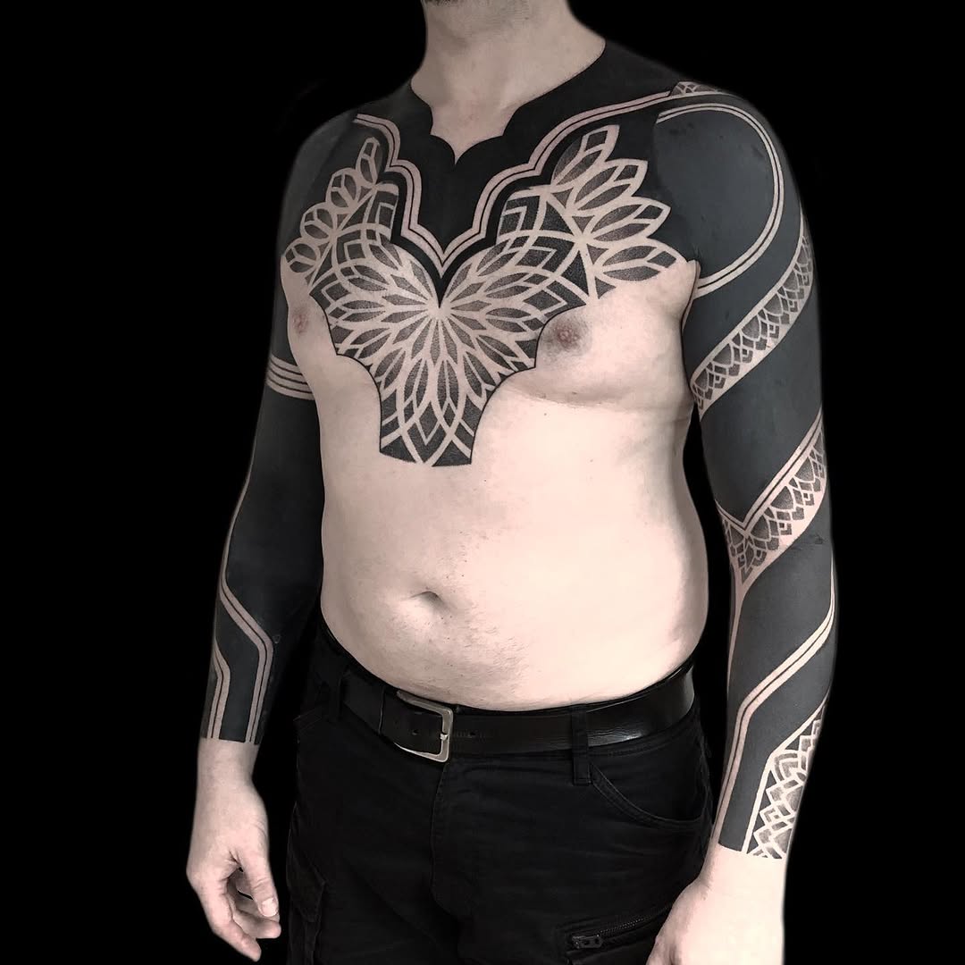 Large symmetrical mandala-style chest piece with geometric linework and ornamental patterning extending down both arms.