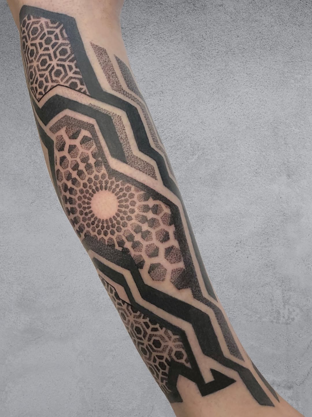 Geometric sleeve tattoo with nested hexagonal patterns, dotwork stippling, concentric circles, and symmetrical angular black linework on forearm.
