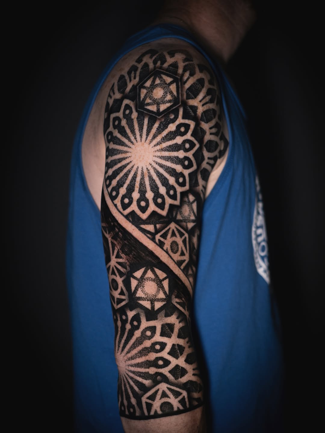 Geometric mandala sleeve tattoo with radiating sunburst patterns, hexagonal elements, and dotwork stippling on upper arm.