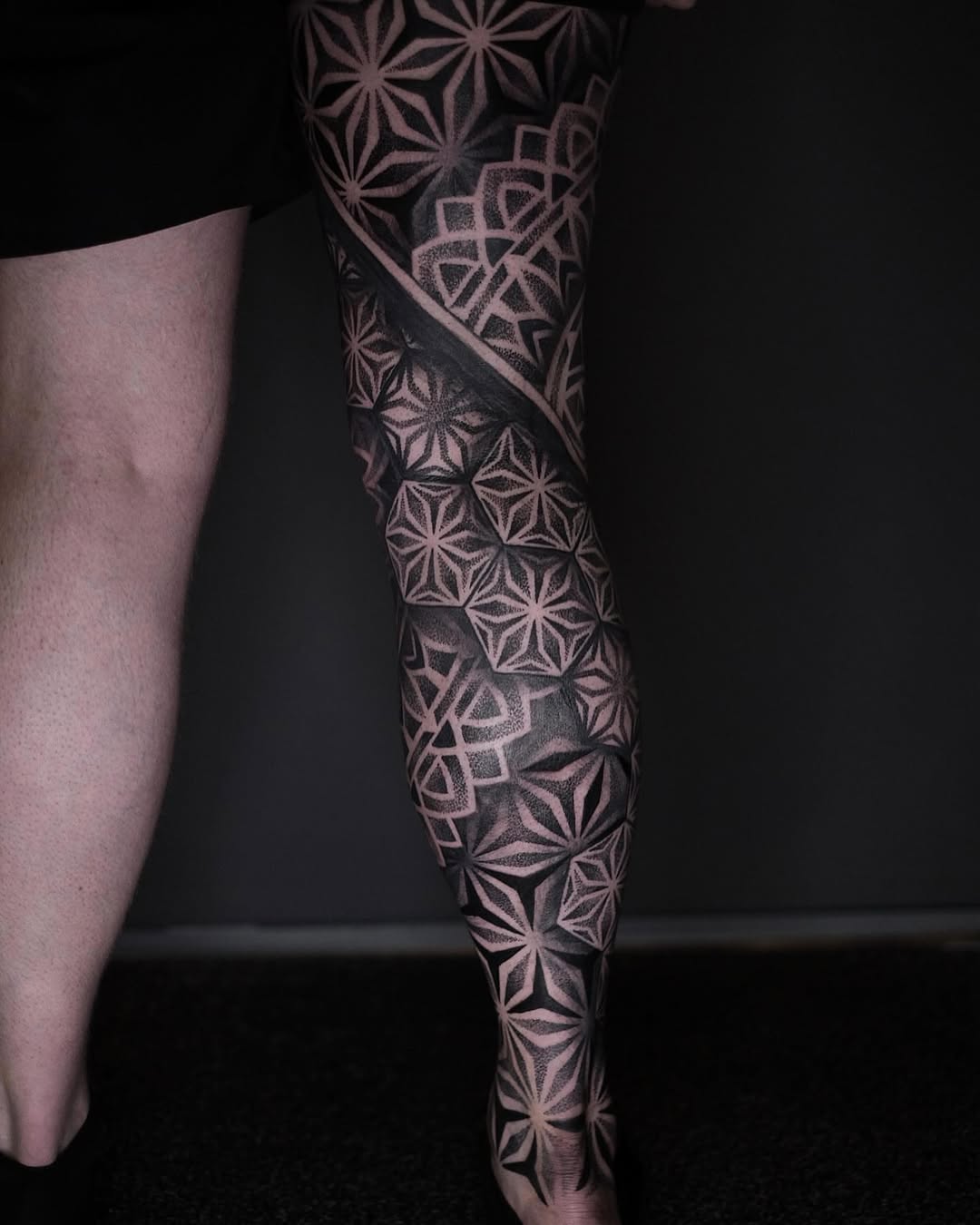 Full leg sleeve with repeating geometric flower patterns and ornamental mandala-inspired motifs in black and grey dotwork.