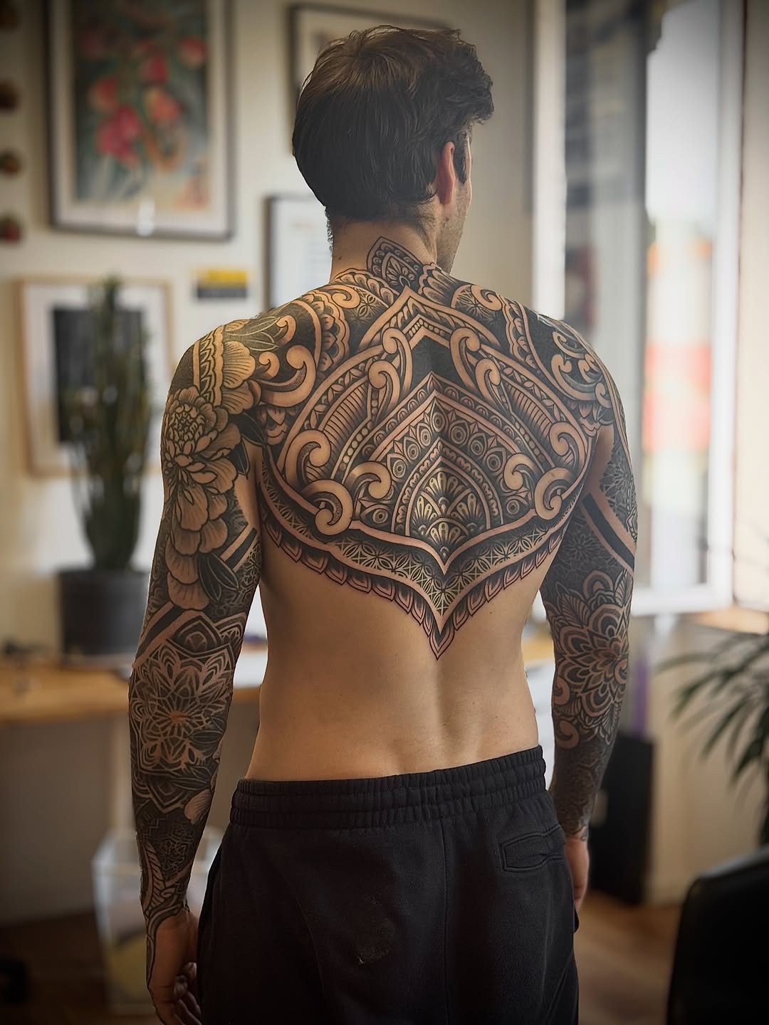 Large ornamental mandala with symmetrical patterning covers back and shoulders with intricate dotwork and linework detail.