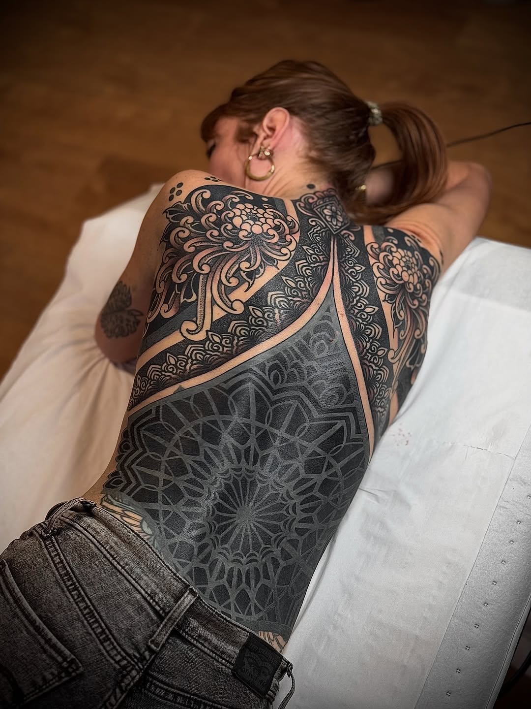 Large-scale geometric mandala and ornamental symmetrical designs covering the upper back and shoulders in black ink.