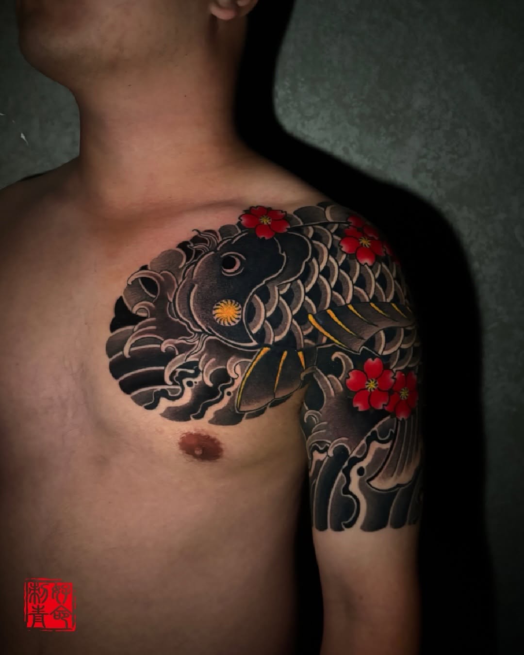 Large-scale Japanese koi fish with ornamental scales, red flowers, and decorative scrollwork on chest and shoulder.