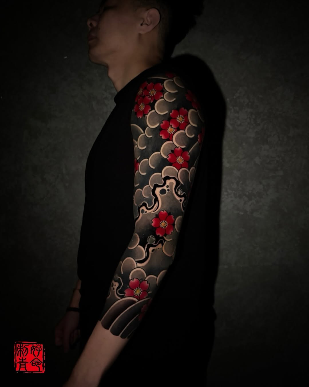 Full sleeve tattoo featuring red flowers, crescent moons, ornamental scrollwork, and flowing wave patterns in Japanese aesthetic on the arm.