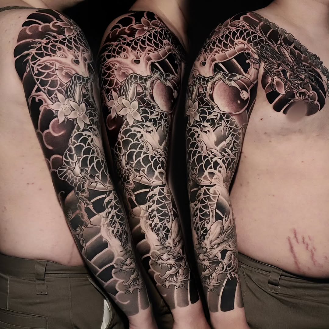 Full-sleeve Japanese dragon tattoo with koi fish, scales, flowers, and ornamental waves in black and grey on both arms.