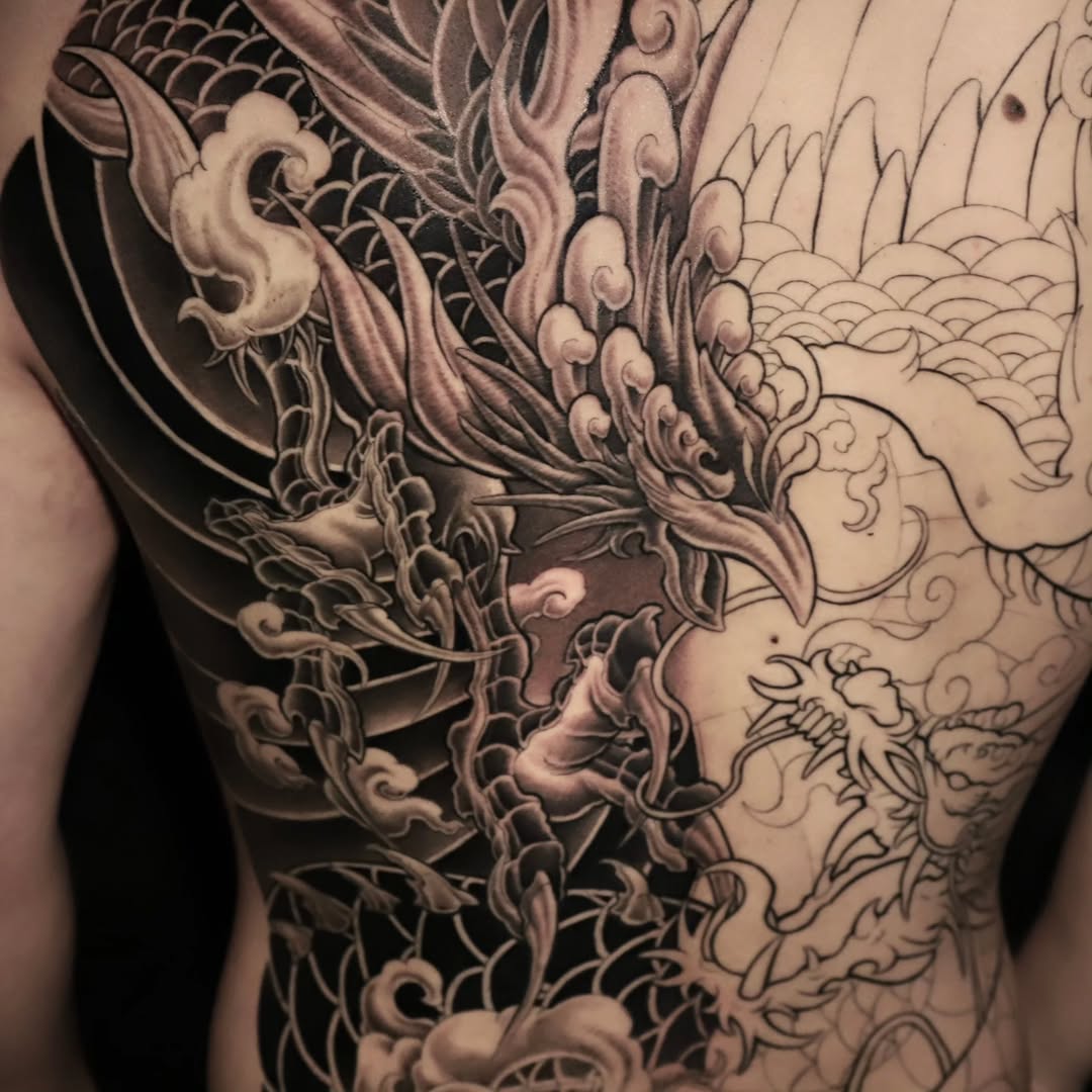 Large-scale Japanese dragon with ornamental clouds and flowing decorative elements covering the upper back and shoulder.