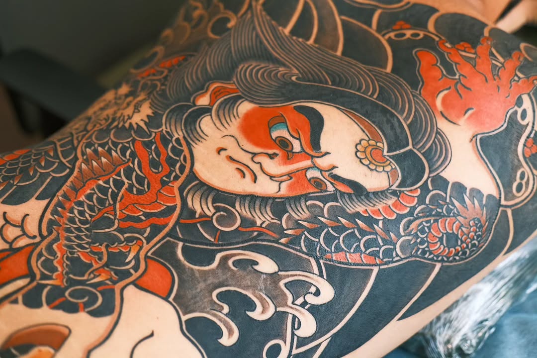 Large-format Japanese-inspired composition featuring an oni mask with red and black pigmentation, intricate dragon and floral elements on arm.