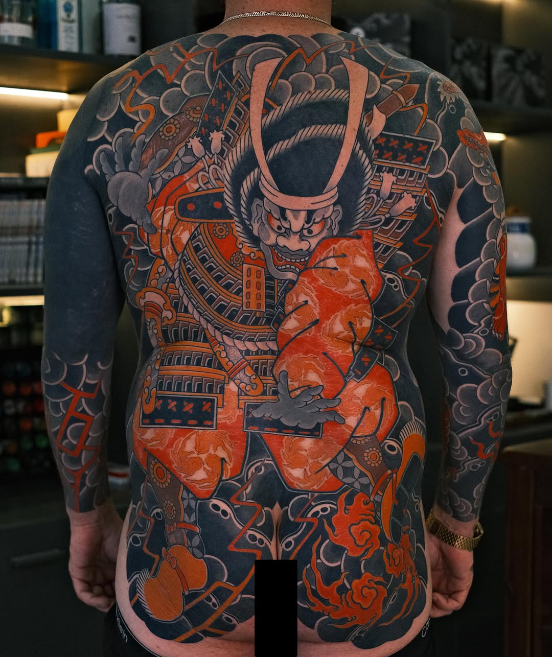 Large-scale Japanese back piece featuring an oni demon in red and black with ornamental clouds, floral motifs, and decorative elements.