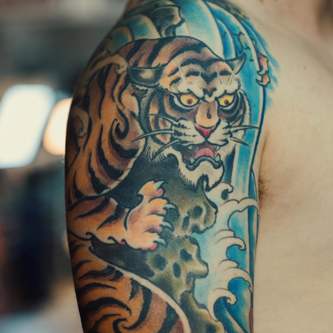 Tiger head with ornamental blue wave background and decorative scrollwork on upper arm.