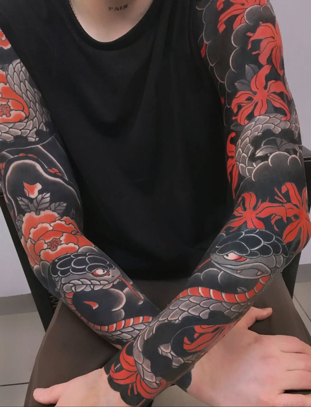 Full sleeve tattoo featuring red and gray Japanese dragons, peonies, and floral motifs on black background on both arms.