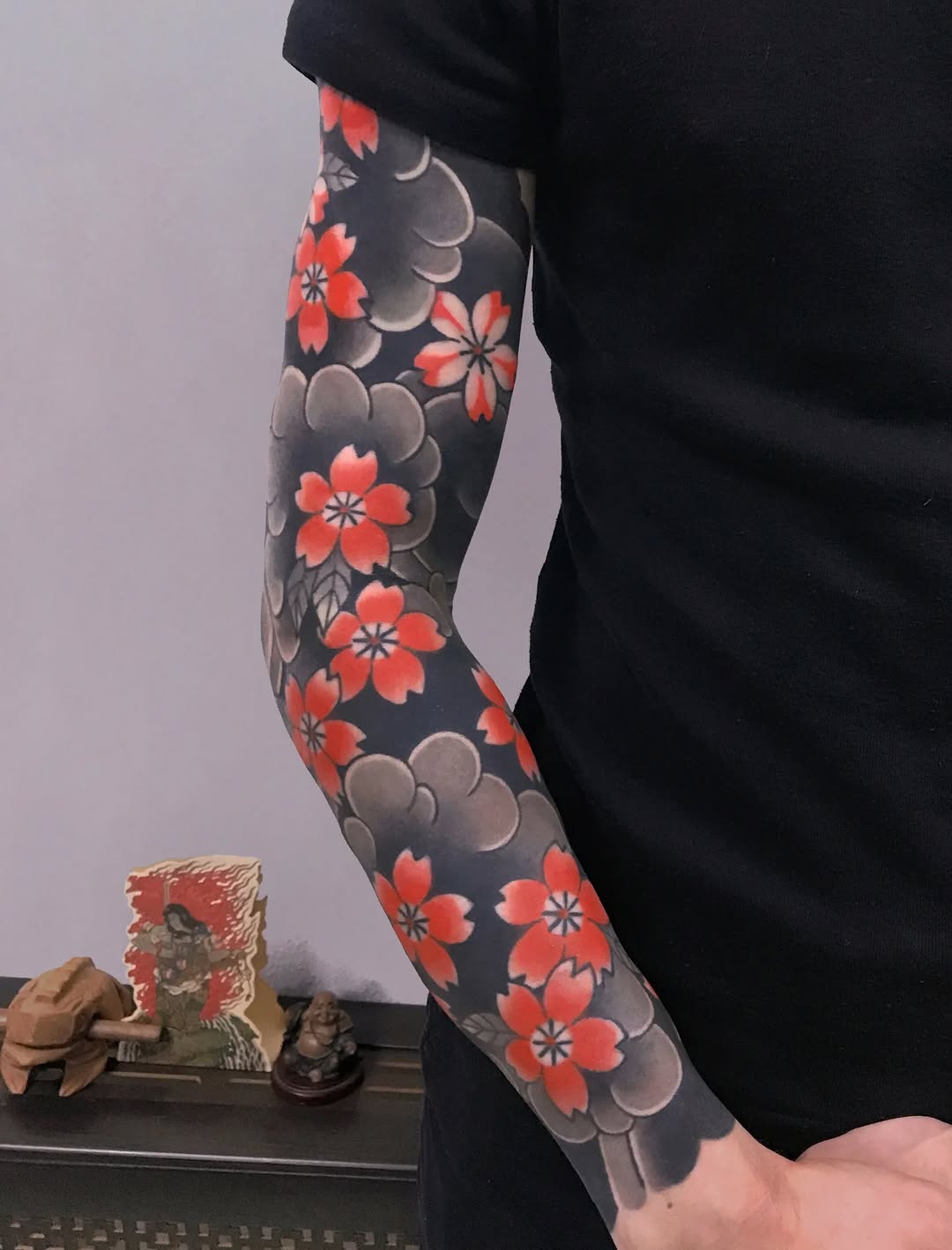 Full-sleeve tattoo featuring red flowers and grey clouds on dark background, covering forearm and upper arm.