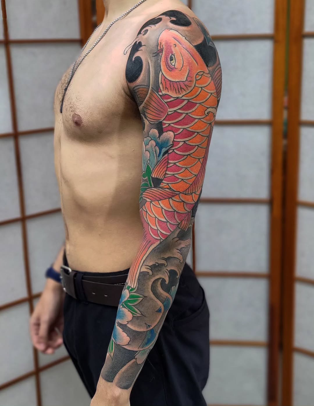 Large koi fish sleeve tattoo in orange and red tones with water and floral elements, extending from shoulder to forearm.