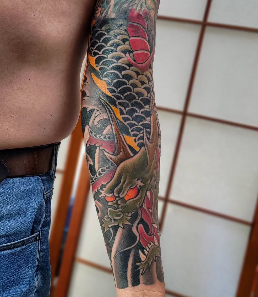 Large-format koi fish with flowing scales, waves, and floral elements in full sleeve composition on forearm.
