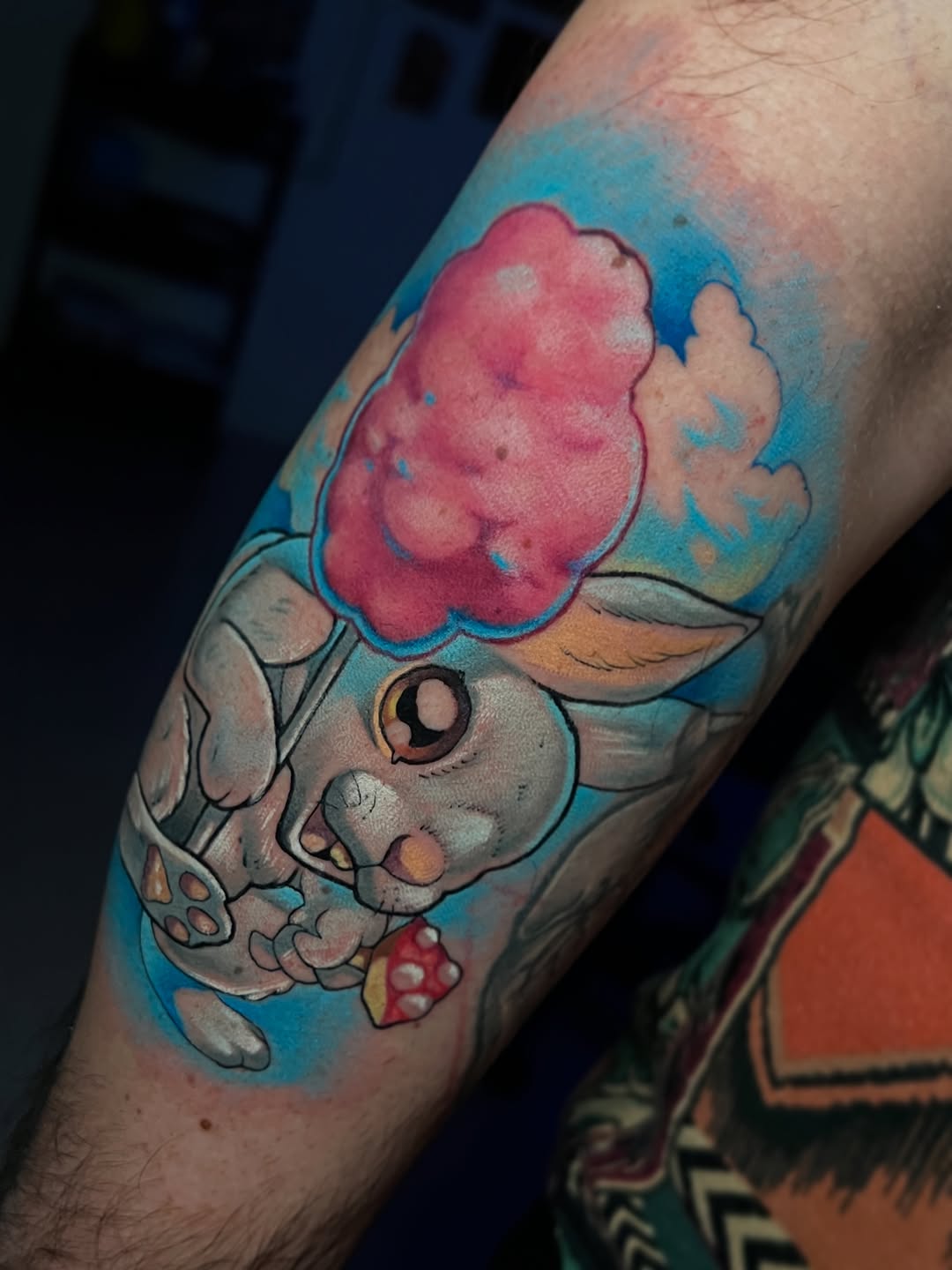 Cartoon elephant character holding a pink cotton candy cone against a blue sky background on the forearm.