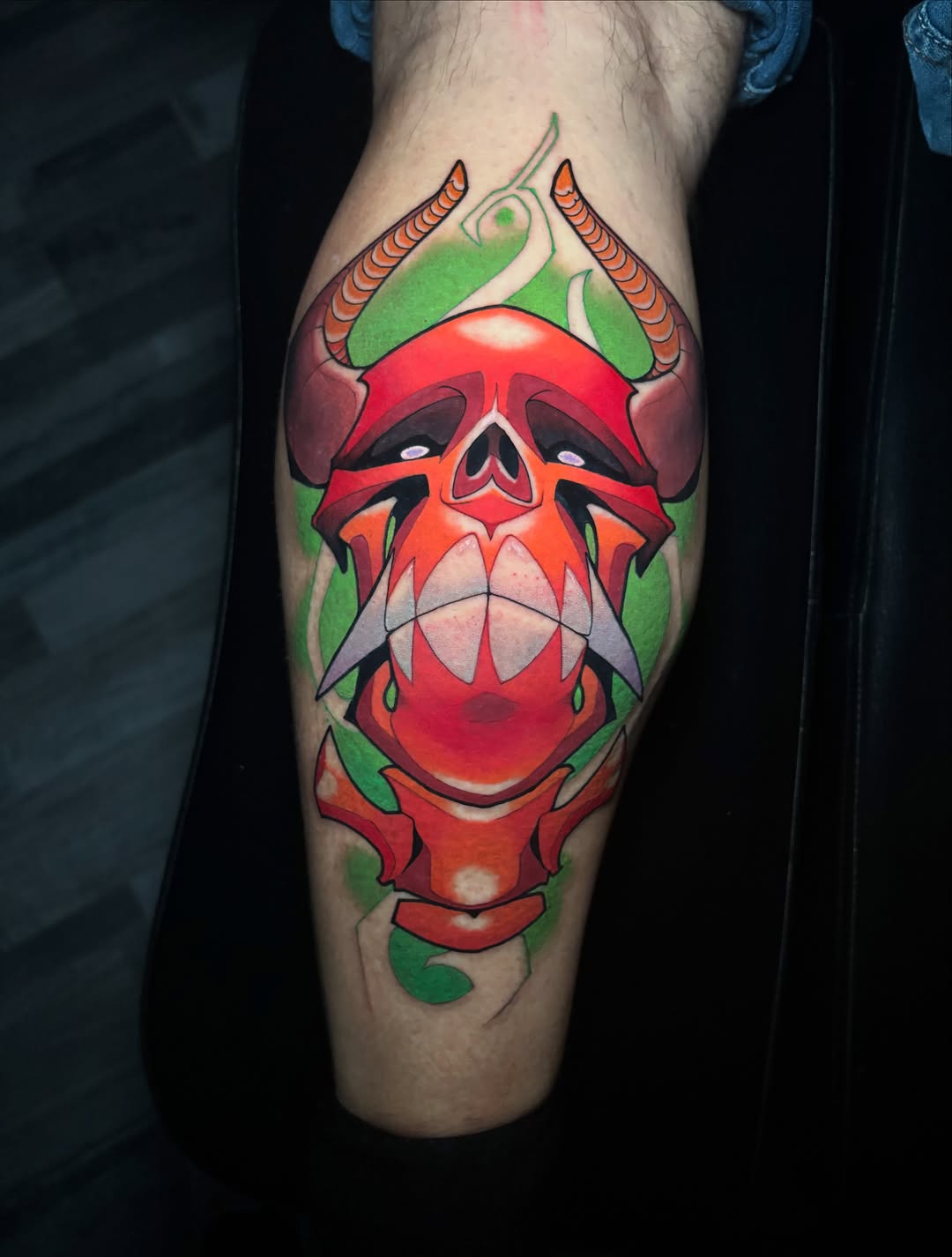 Demonic red creature head with horns, green background, and exaggerated 3D features on the calf.