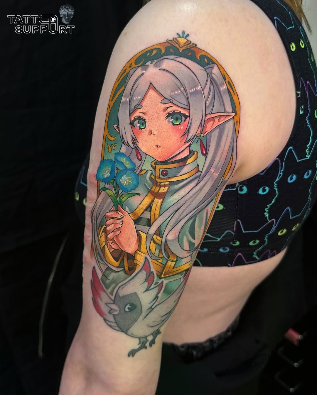 Anime elf character with silver hair holding blue flowers, wearing ornate gold armor, upper arm placement.