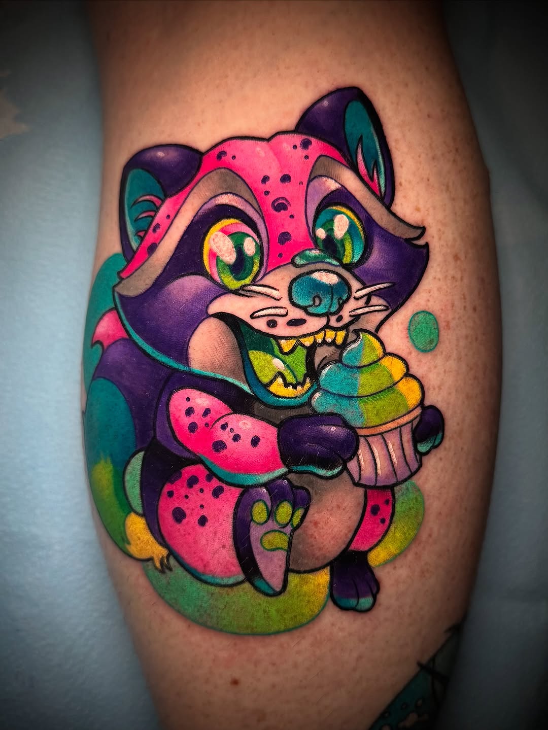 Colorful cartoon cat character with purple face, pink spotted body, holding striped candy, on calf.